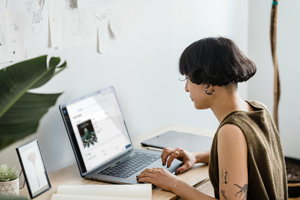 Mujer promotora de música trabajando en una laptop en un escritorio con plantas y bocetos en la pared.