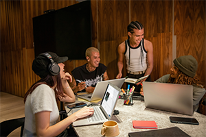 Grupo de jóvenes profesionales de un sello discográfico colaborando en una reunión creativa con laptops y cuadernos sobre la mesa para promocionar un single en Caster.